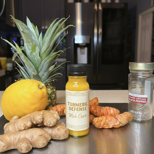 Bottles of yellow juice with a pineapple, lemon, ginger, and black pepper jar on a kitchen counter.